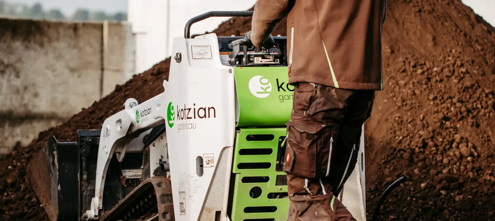 Kompaktlader mit Kotzian-Logo vor einem Erdhaufen