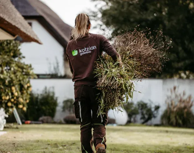 Mitarbeiterin trägt Schnittgut durch einen Garten